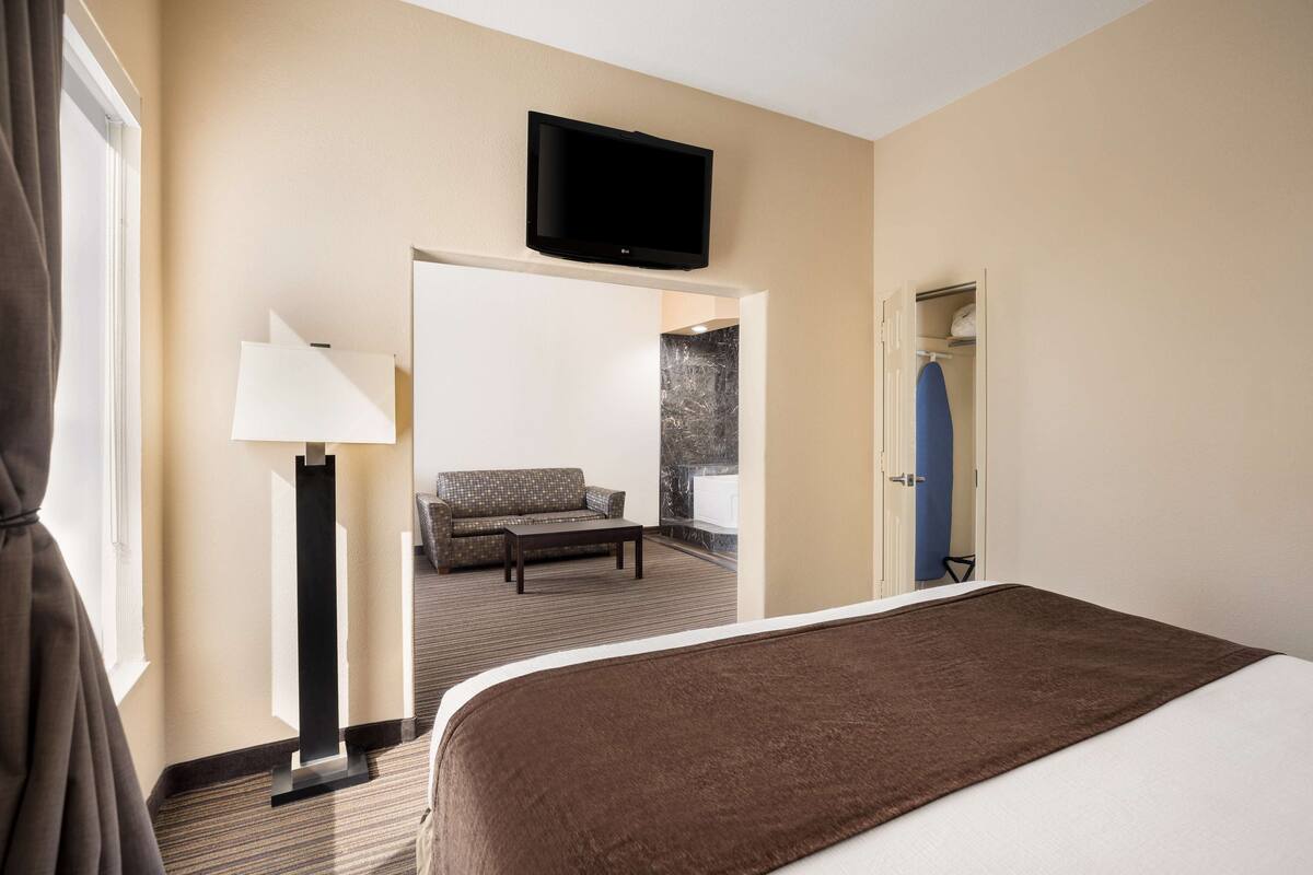 A hotel room with a bed, a flat-screen TV mounted above the bed, a sofa, a coffee table, and a lamp.