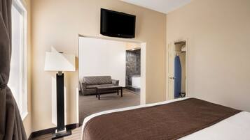 A hotel room with a bed, a flat-screen TV mounted above the bed, a sofa, a coffee table, and a lamp.