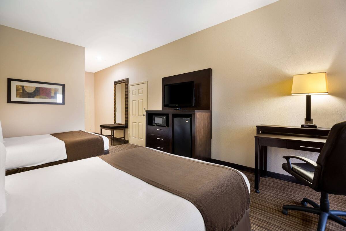 A hotel room with two beds, a desk, a chair, a television, a microwave, and a refrigerator.