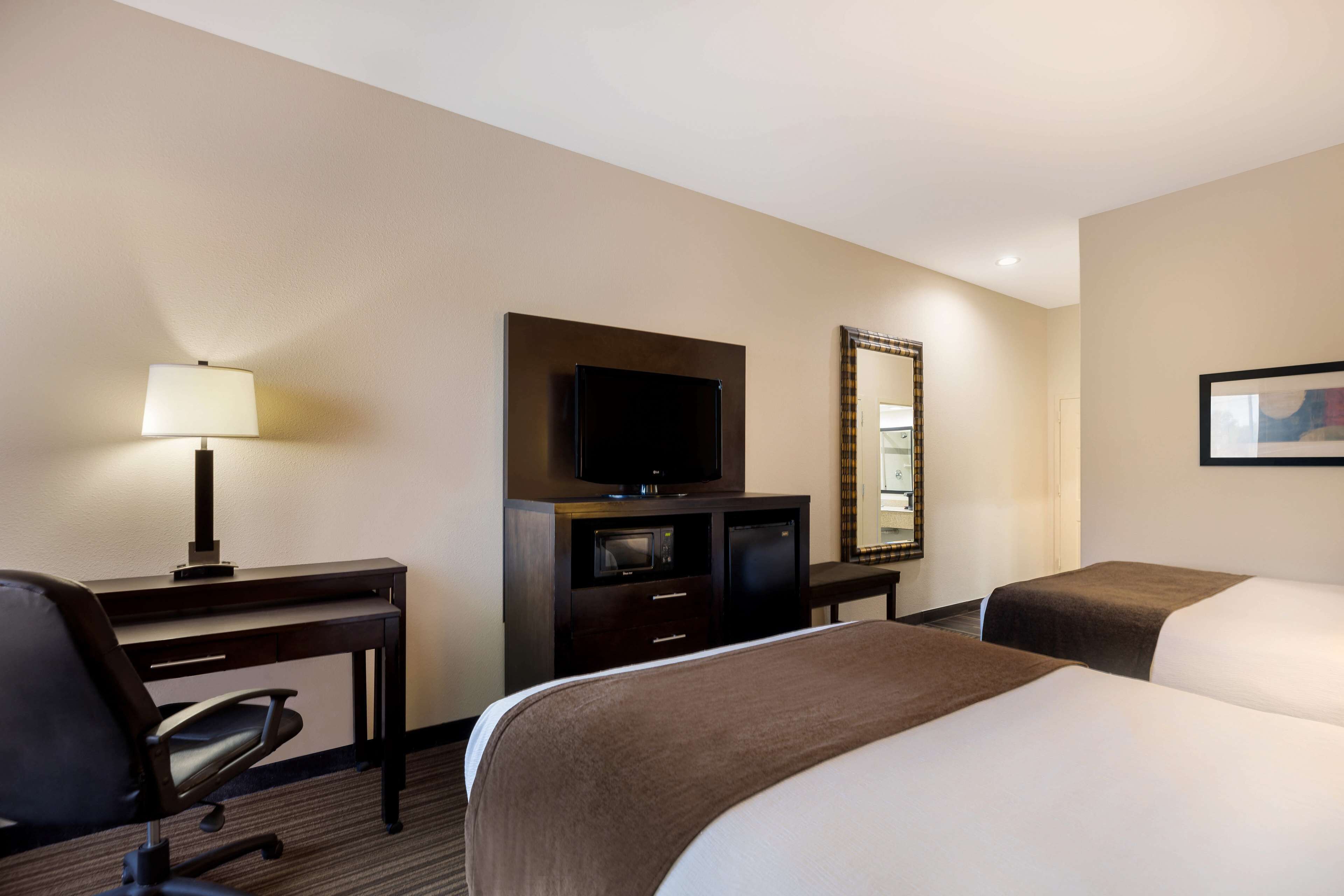 A hotel room with a desk, a television, a mirror, and two beds.