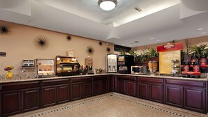 Een ontbijtruimte in een hotel met een koffiehoek, een koelkast, een magnetron en diverse etenswaren.