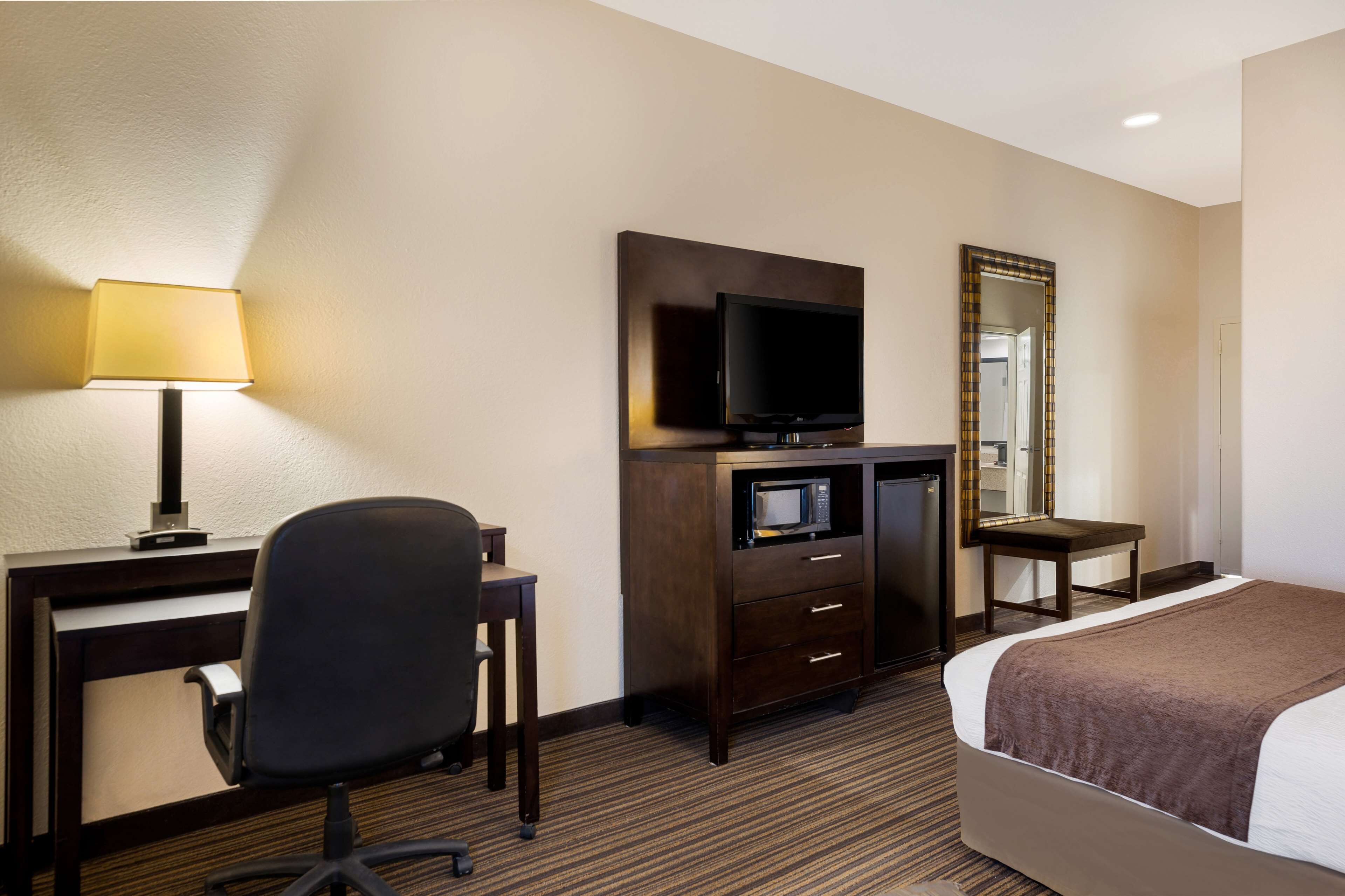 Een hotelkamer met een bed, bureau, stoel, televisie, magnetron en spiegel.
