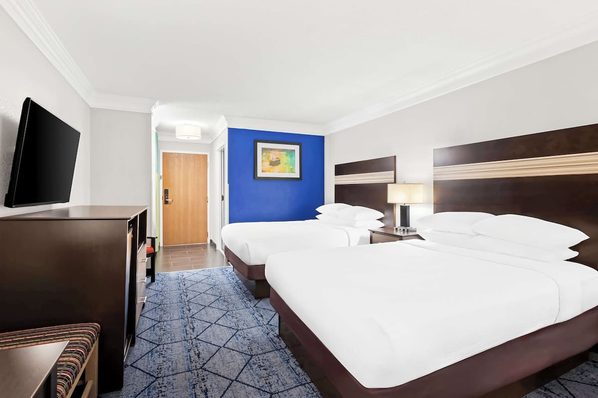 A hotel room with a large bed, a TV, a desk, and a blue accent wall.