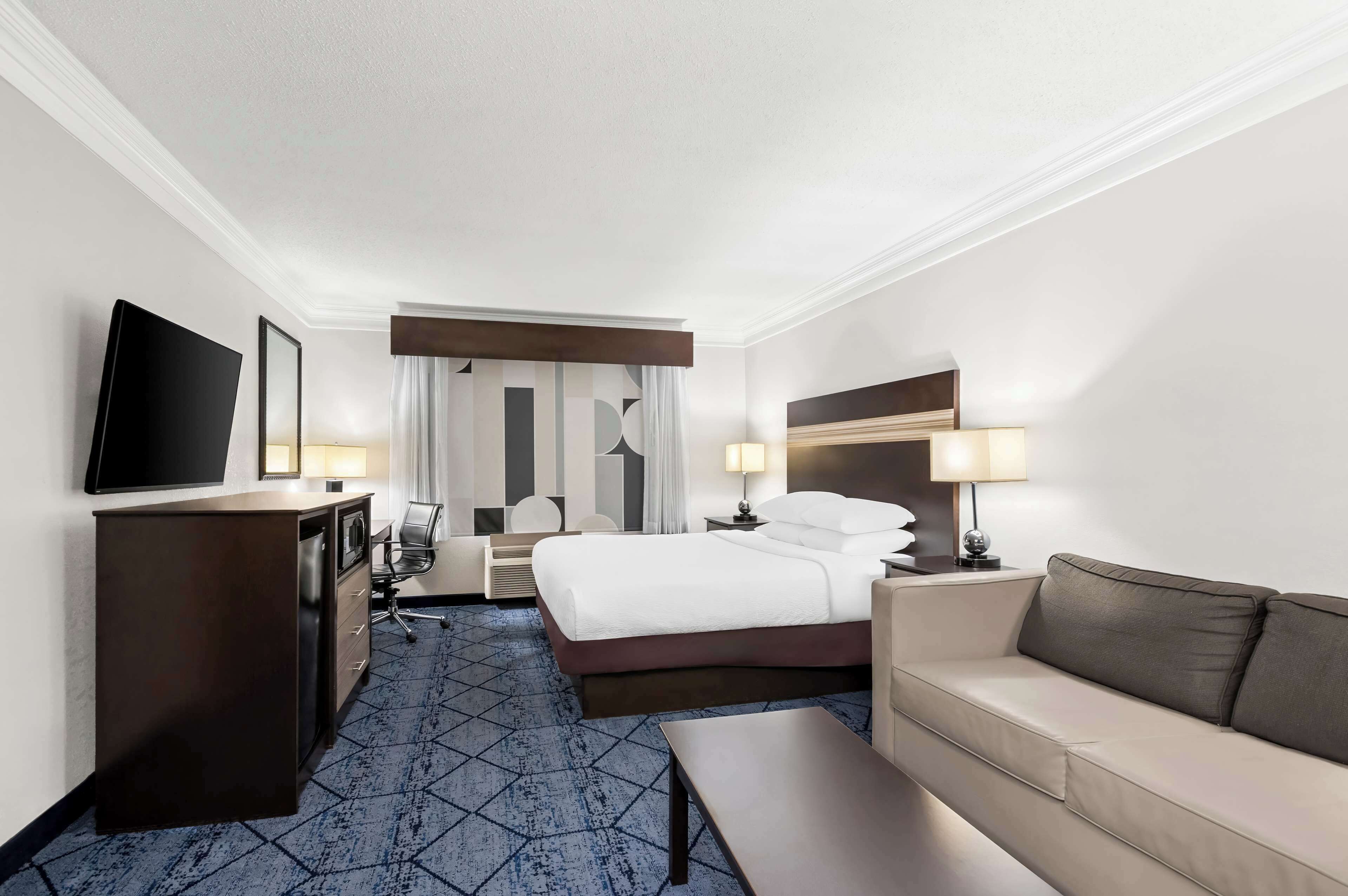 A hotel room with a bed, a desk, a TV, a sofa, and a lamp.