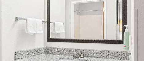 Un baño con lavamanos de encimera de granito, un espejo grande y un perchero con dos toallas blancas.