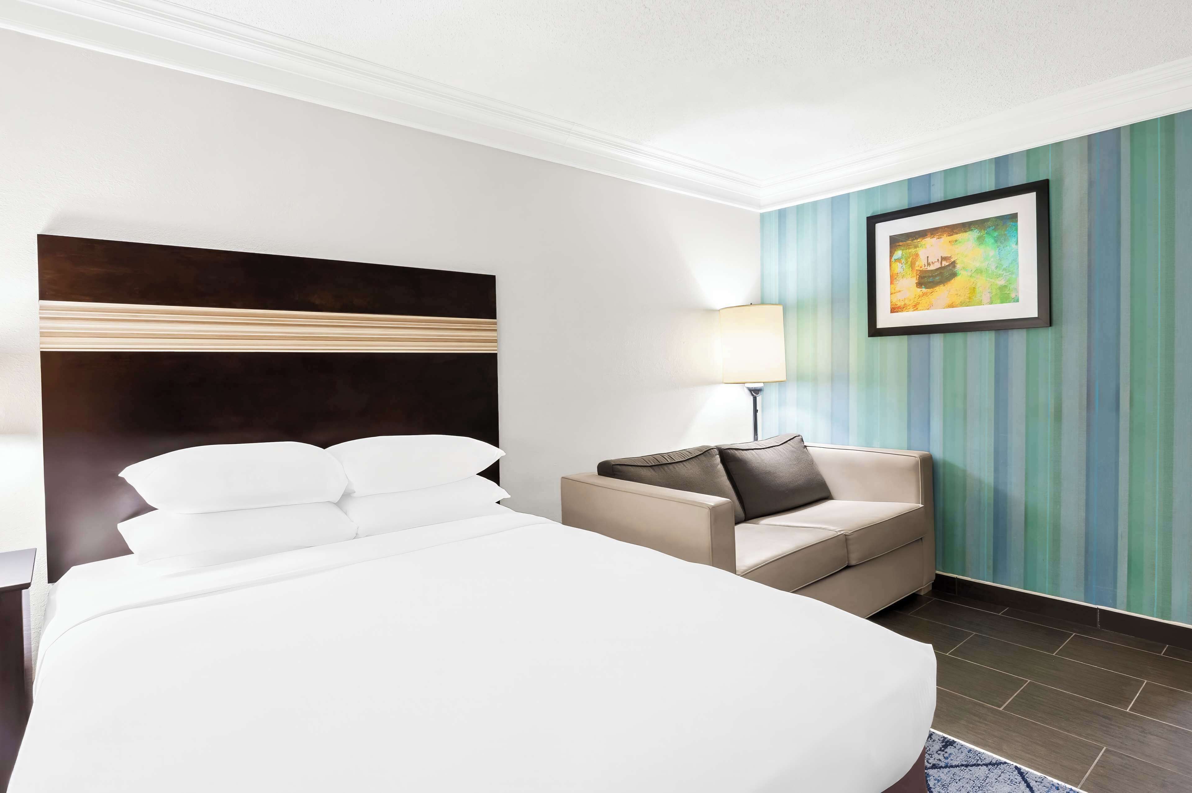 Een hotelkamer met een groot bed, een sofa, een nachtkastje, een lamp en een schilderij aan de muur.