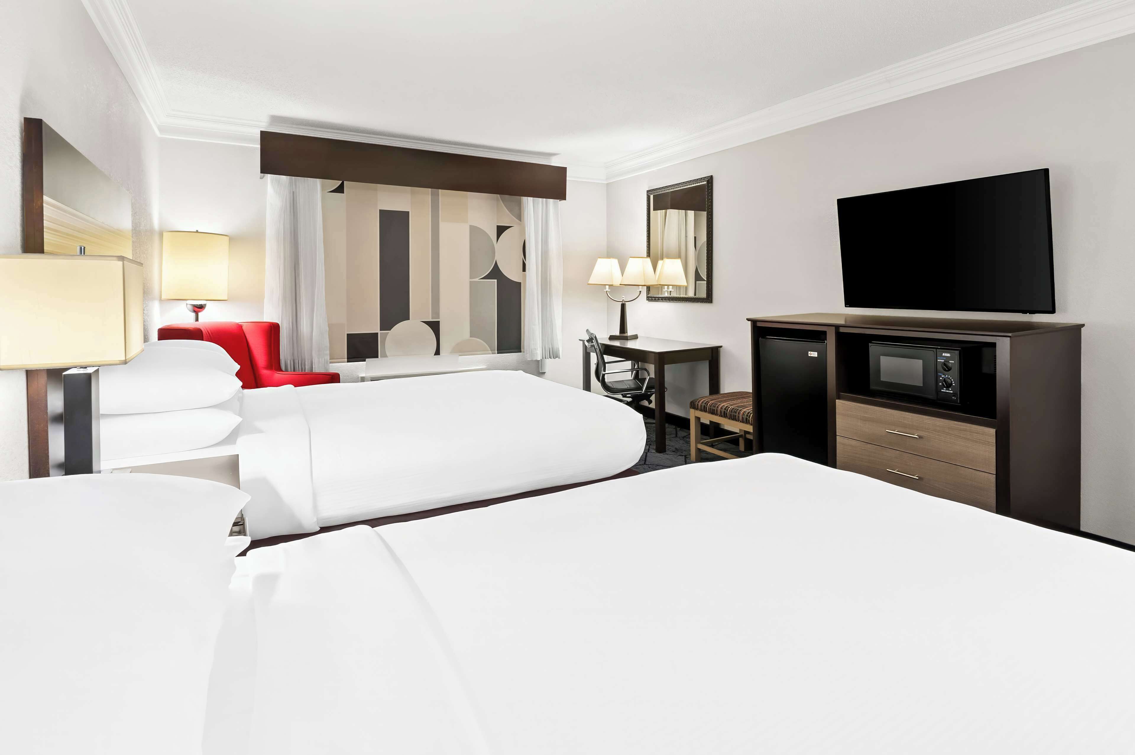 A hotel room with two beds, a desk with a chair, a television, and a minibar.
