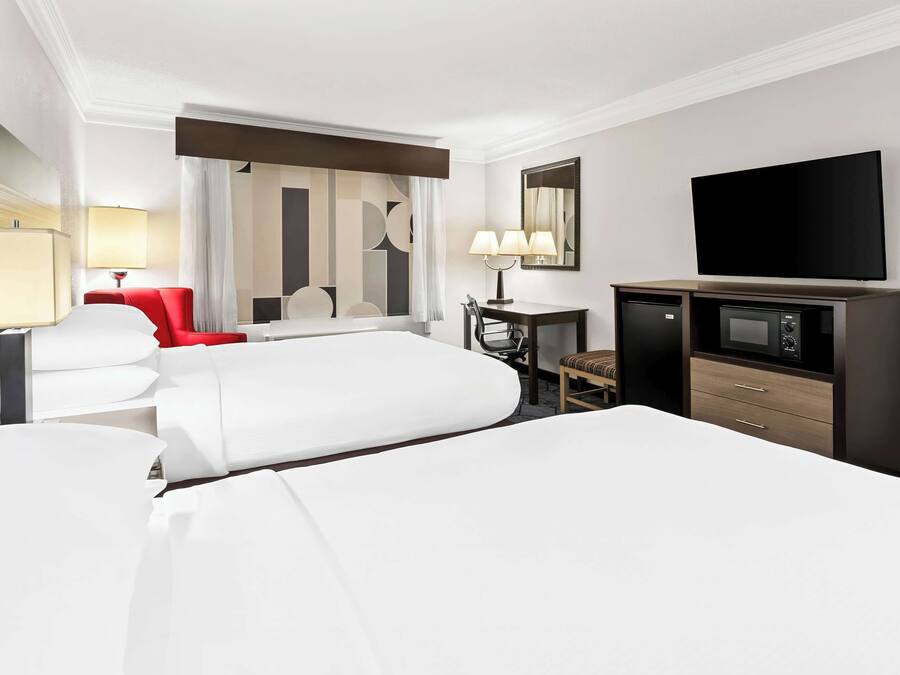 A hotel room with two beds, a desk with a chair, a television, and a minibar.