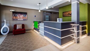A modern reception area with a reception desk, a red sofa, a unique white vase, and a cityscape painting on the wall. - Best Western Slidell Hotel (Slidell)