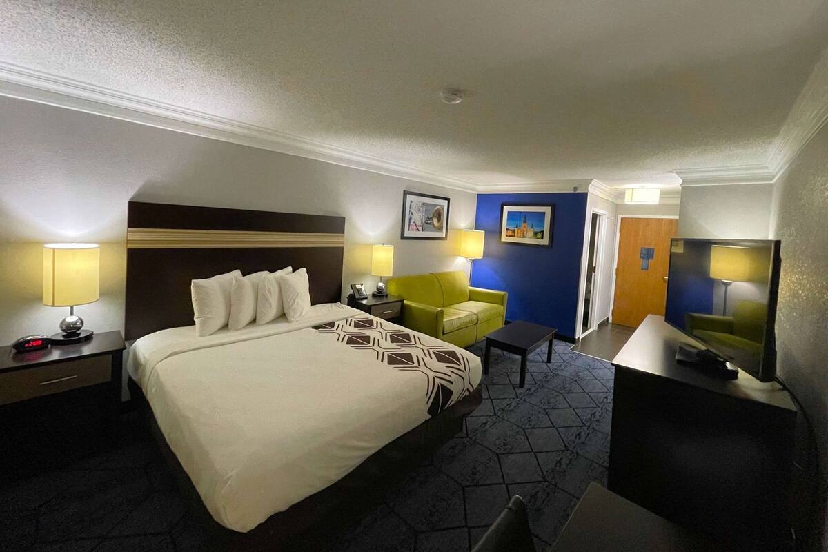 A hotel room with a bed, bedside tables, a desk, a chair, and a television.