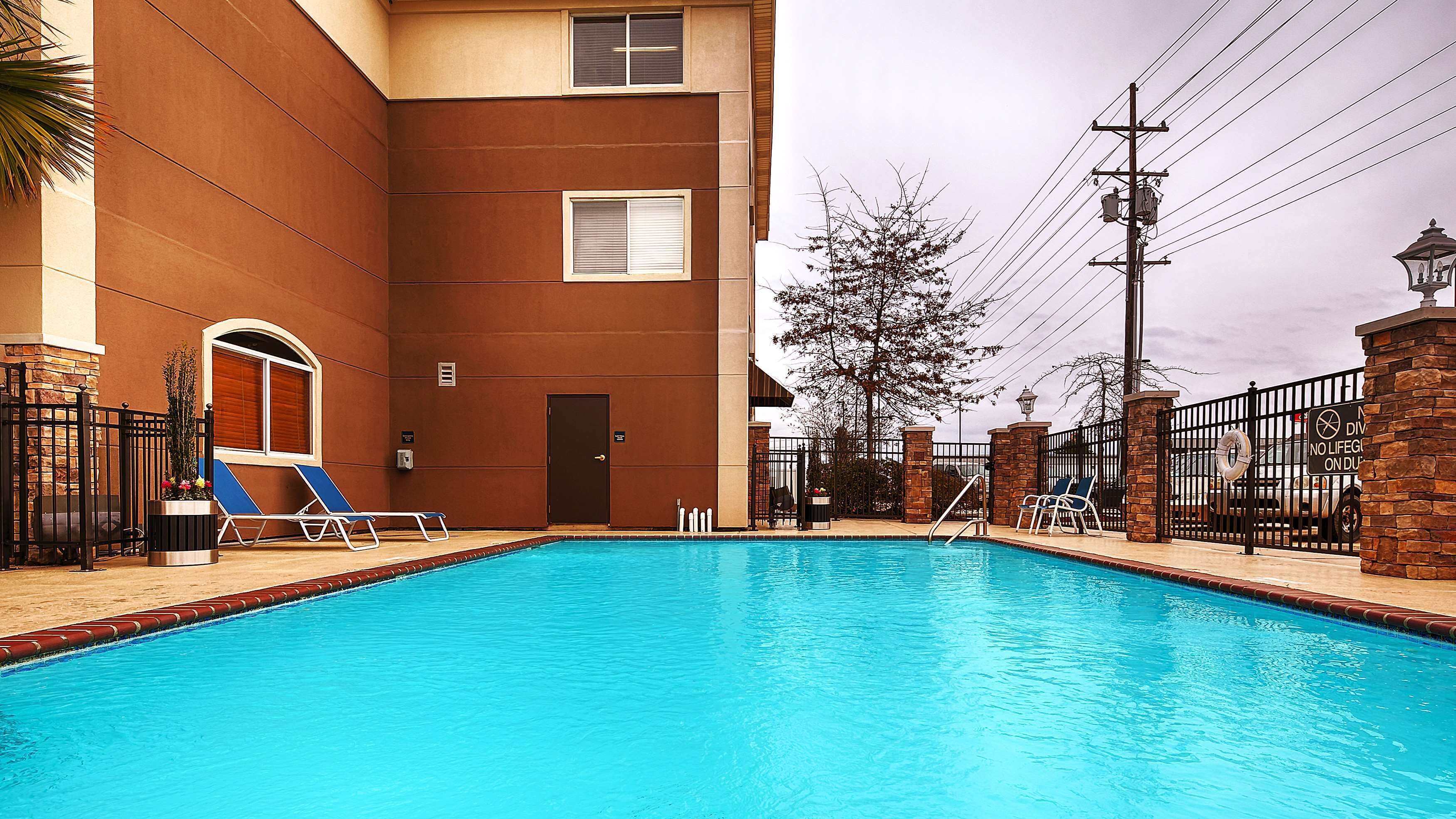 A swimming pool with a clear blue water, surrounded by a brick wall and a metal fence.