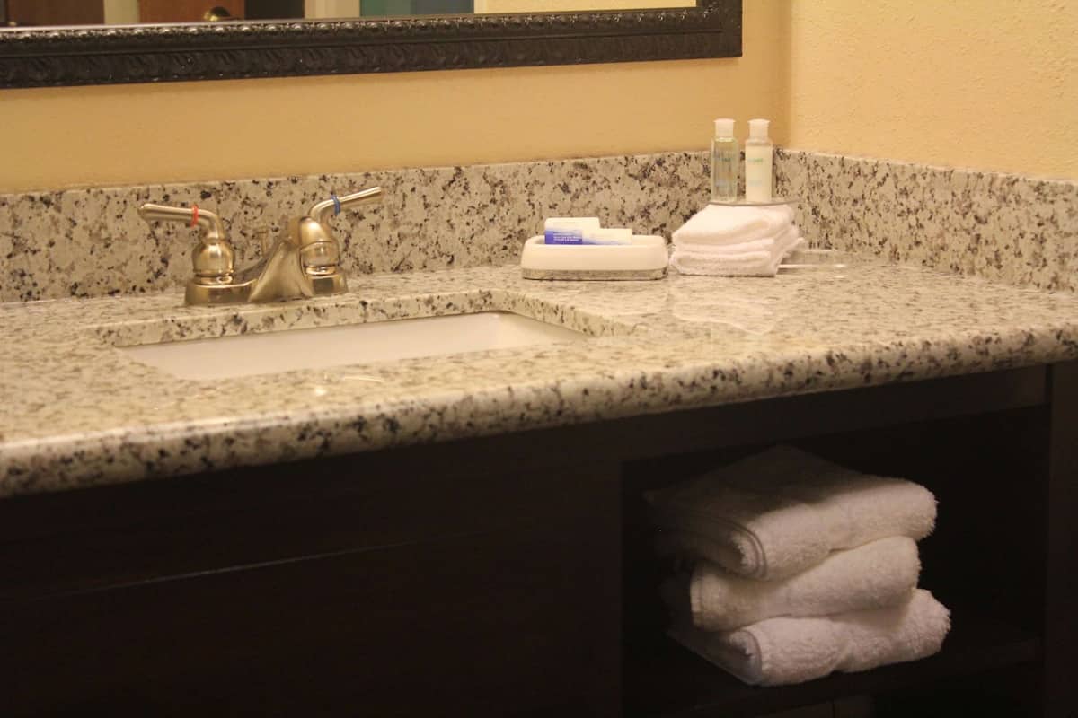 A bathroom with a granite countertop, a sink, a mirror, and a towel rack with folded towels.