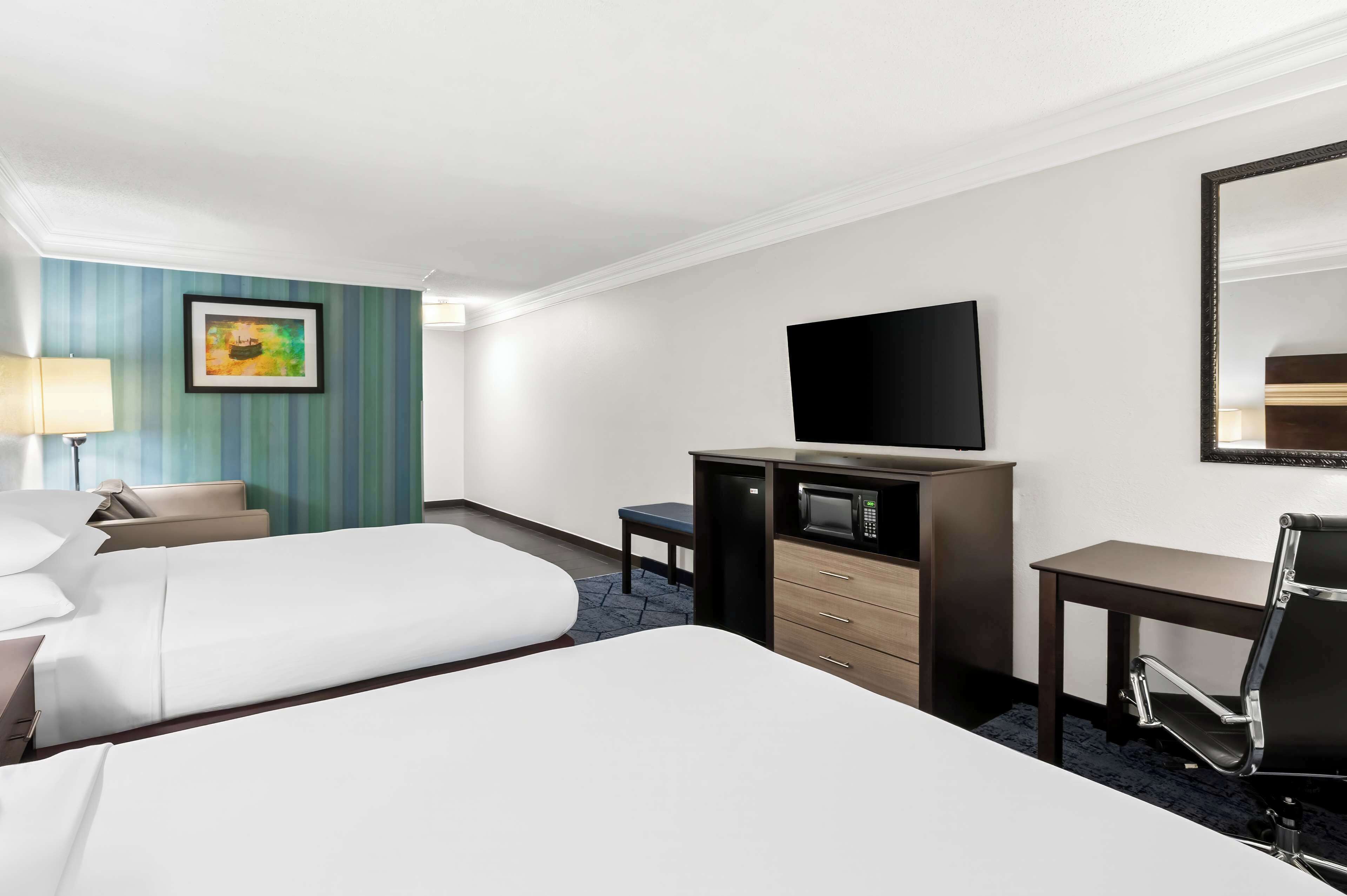 A hotel room with two beds, a desk, a chair, a TV, and a small table.