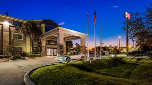 A hotel entrance with a covered driveway, flagpoles, and a parking area. - Best Western Slidell Hotel (Slidell)
