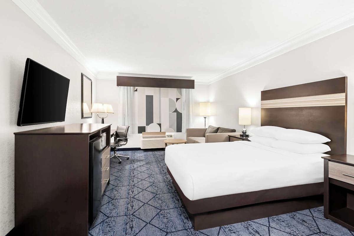 A hotel room with a large bed, a desk with a chair, a television, and two lamps.