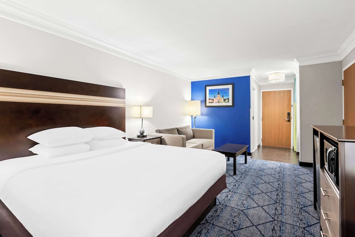 A hotel room with a large bed, a desk, a chair, a sofa, a lamp, and a picture on the wall.