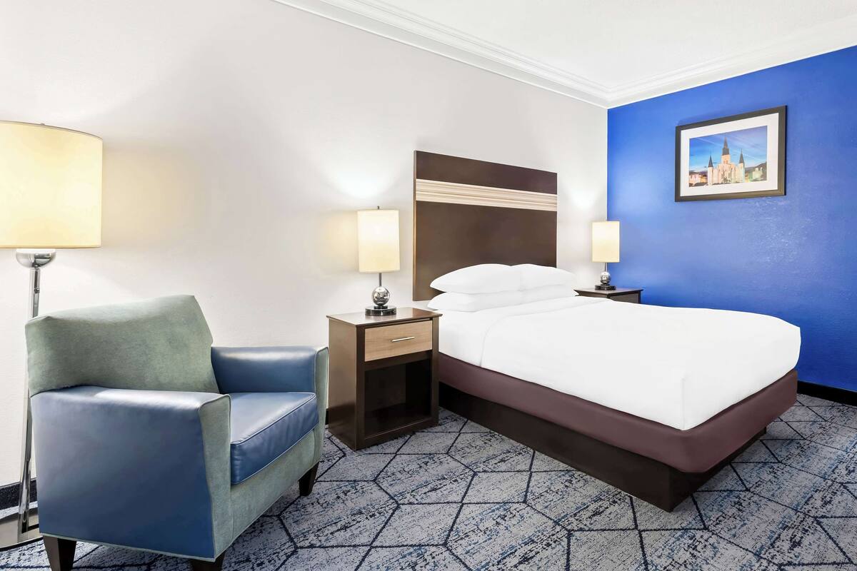 A hotel room with a bed, a chair, a nightstand, and a lamp.