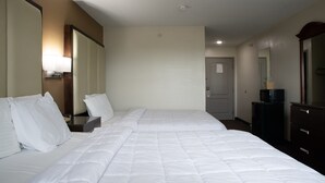 Et hotelværelse med to senge, et skrivebord med lampe, et kommode, et fjernsyn og en dør.