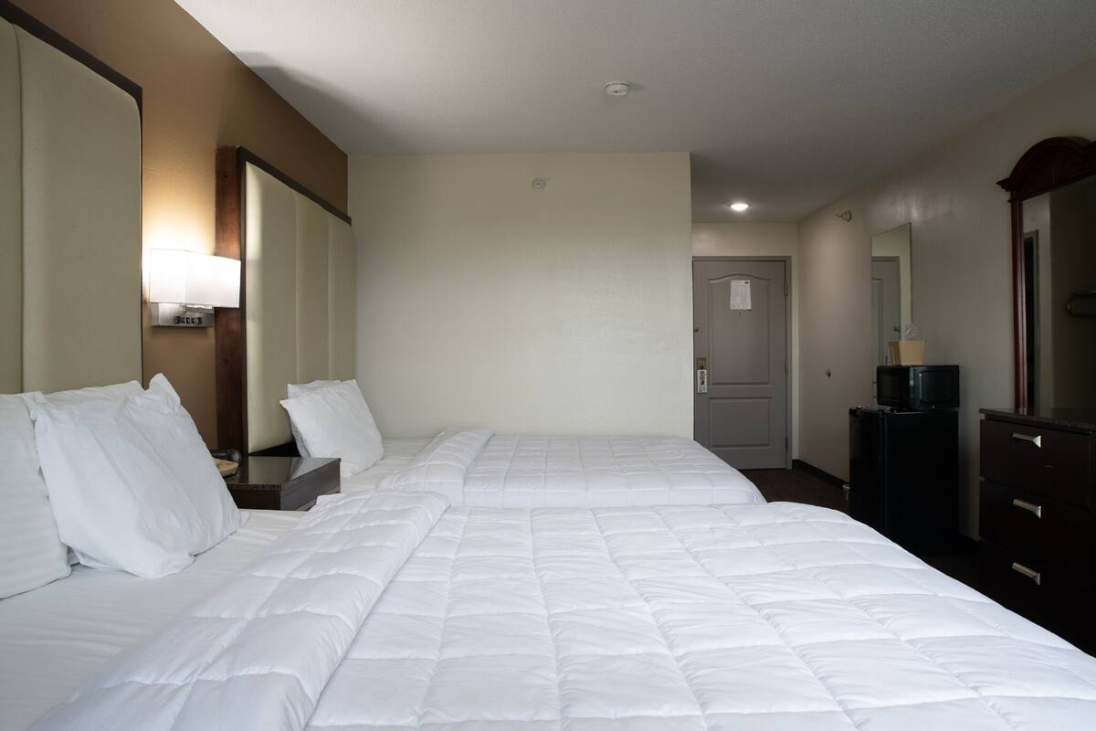 A hotel room with two beds, a desk with a lamp, a dresser, a television, and a door.