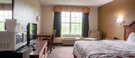 Habitación de hotel con cama, escritorio con televisor, microondas, silla, lámpara y ventana con cortinas.