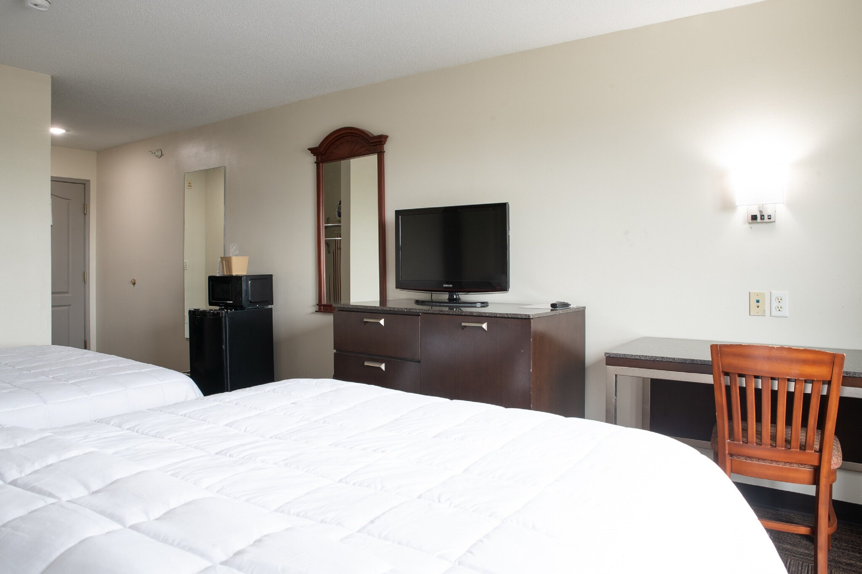 A hotel room with a bed, a desk, a television, and a mirror.