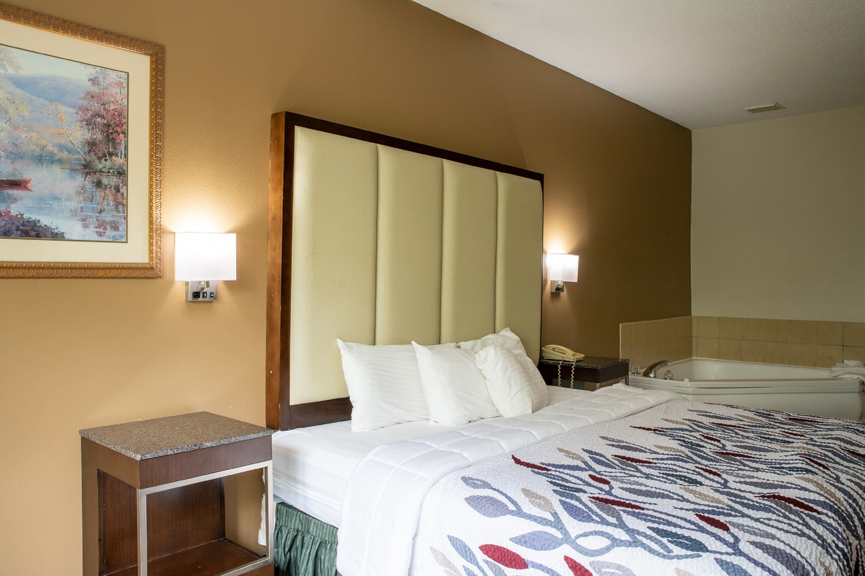 A hotel room with a large bed, two bedside lamps, a nightstand, a telephone, and a bathtub.