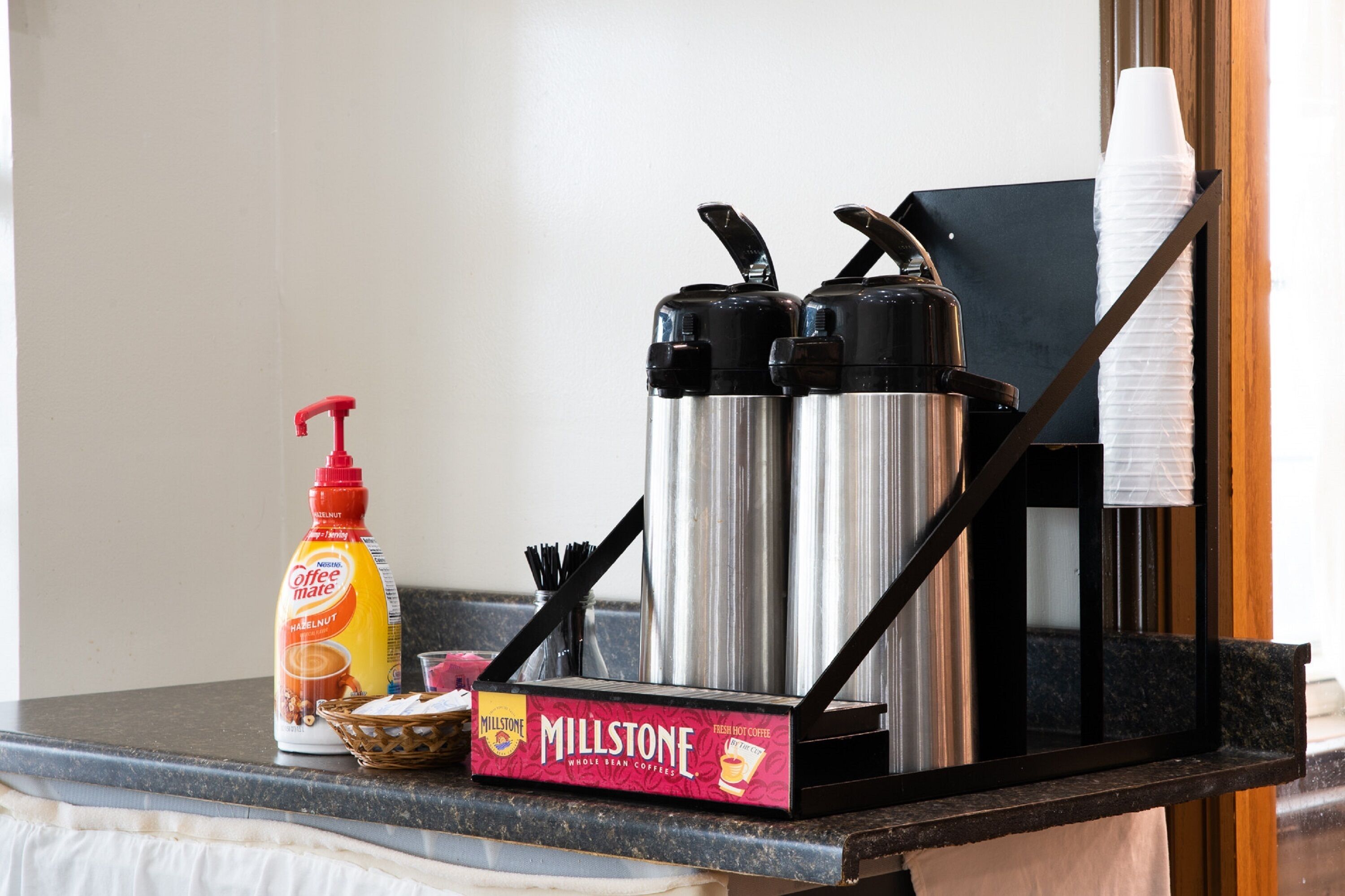 A kitchen counter with a coffee maker, a bottle of coffee creamer, a box of coffee pods, and a thermos.