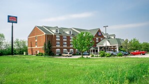 Et Fairbridge Inn & Suites med murstensfacade, mange vinduer og en parkeringsplads med flere biler.