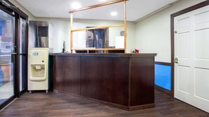 Un espace d’accueil comprenant un comptoir de réception en bois, un distributeur d’eau et une porte vitrée donnant sur l’extérieur.