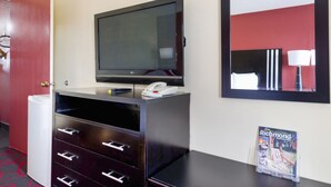 Une chambre d’hôtel équipée d’un téléviseur à écran plat, d’un téléphone, d’un minibar, d’un miroir et d’un présentoir à magazines.