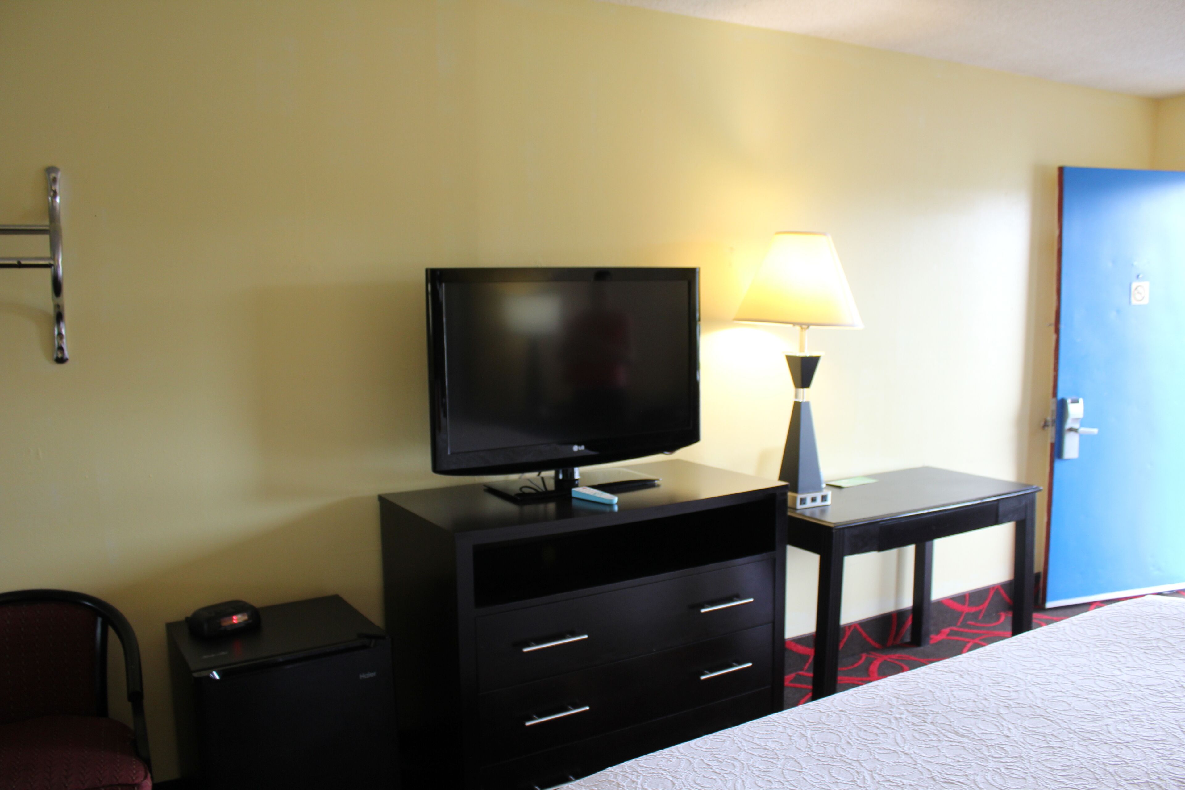 A hotel room with a bed, a TV on a dresser, a lamp, and a door.