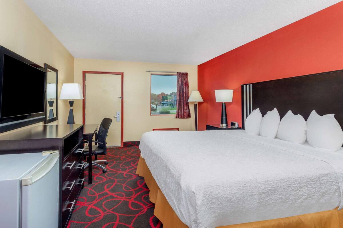 Une chambre d’hôtel avec un lit, un bureau avec une télévision, un réfrigérateur et une fenêtre donnant sur un beau paysage.