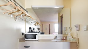 Une salle de bain d’hôtel avec un lavabo blanc, un miroir, un sèche-cheveux et un four à micro-ondes posés sur le comptoir.
