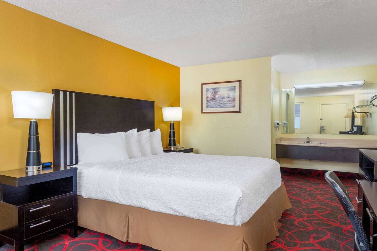 Une chambre d’hôtel comprenant un lit, deux tables de chevet, une commode, un miroir et une salle de bain avec un lavabo et un miroir.
