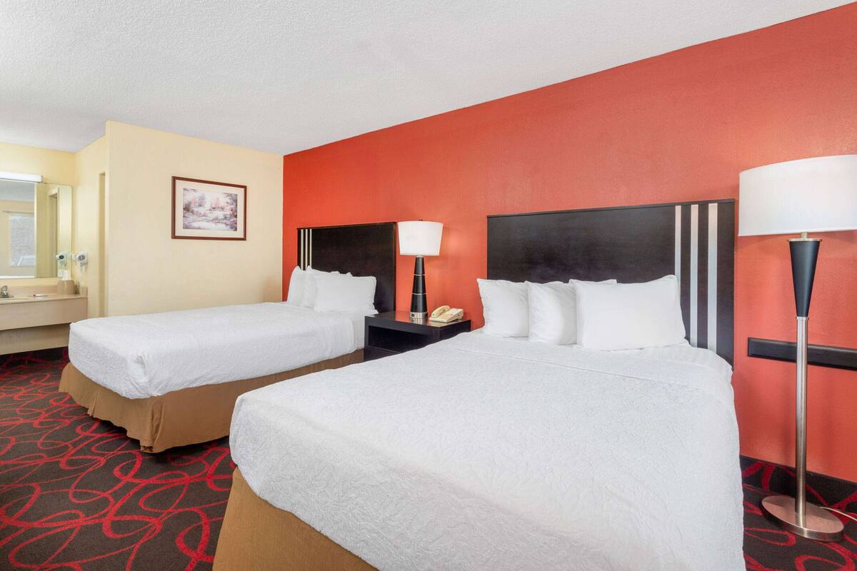 Une chambre d’hôtel avec deux lits, un grand miroir, un tableau et une moquette rouge.