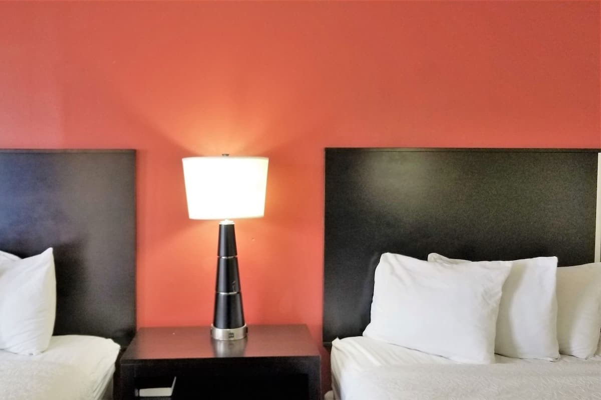 Une chambre d’hôtel avec deux lits, une table de chevet avec une lampe et un mur rouge.