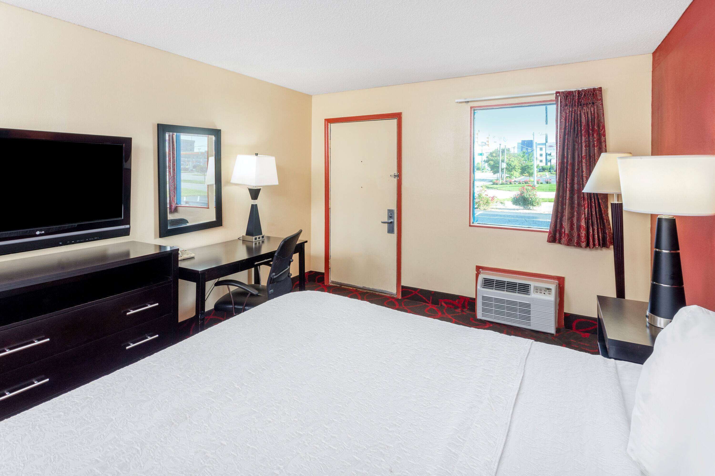 Habitación de hotel con una cama grande, un televisor de pantalla plana, un escritorio con silla, una ventana con vistas y una puerta.