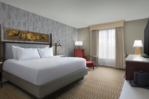 A hotel room with a large bed, a desk, a chair, a painting on the wall, and a window with curtains. - Virginia Crossings Hotel (Glen Allen)