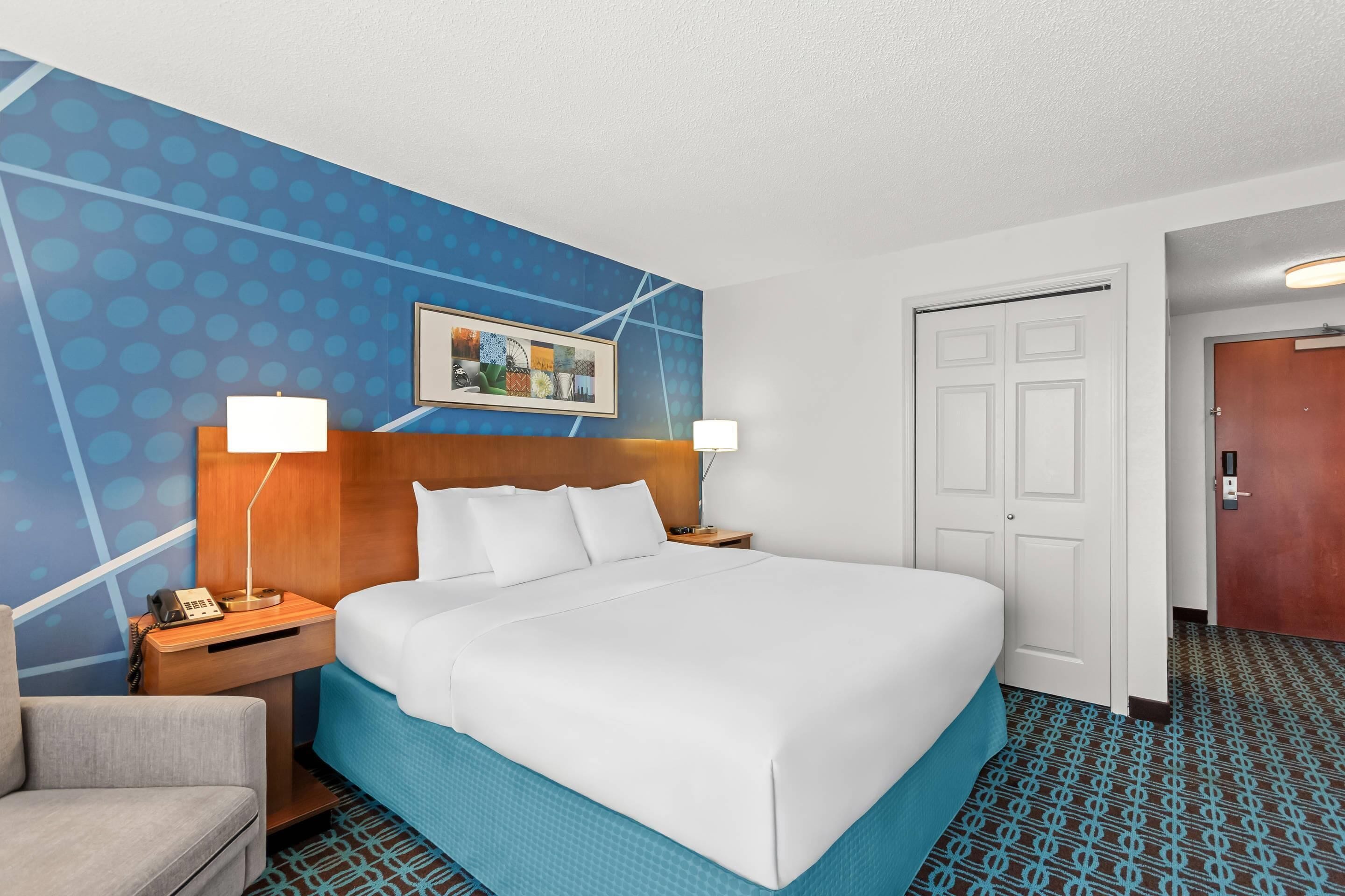 Une chambre d’hôtel avec un grand lit, un bureau avec une lampe, une chaise, une porte et un tapis à motifs.