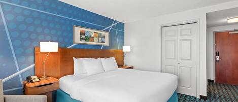 Habitación de hotel con una cama grande, un escritorio con lámpara, una silla, una puerta y una alfombra estampada.