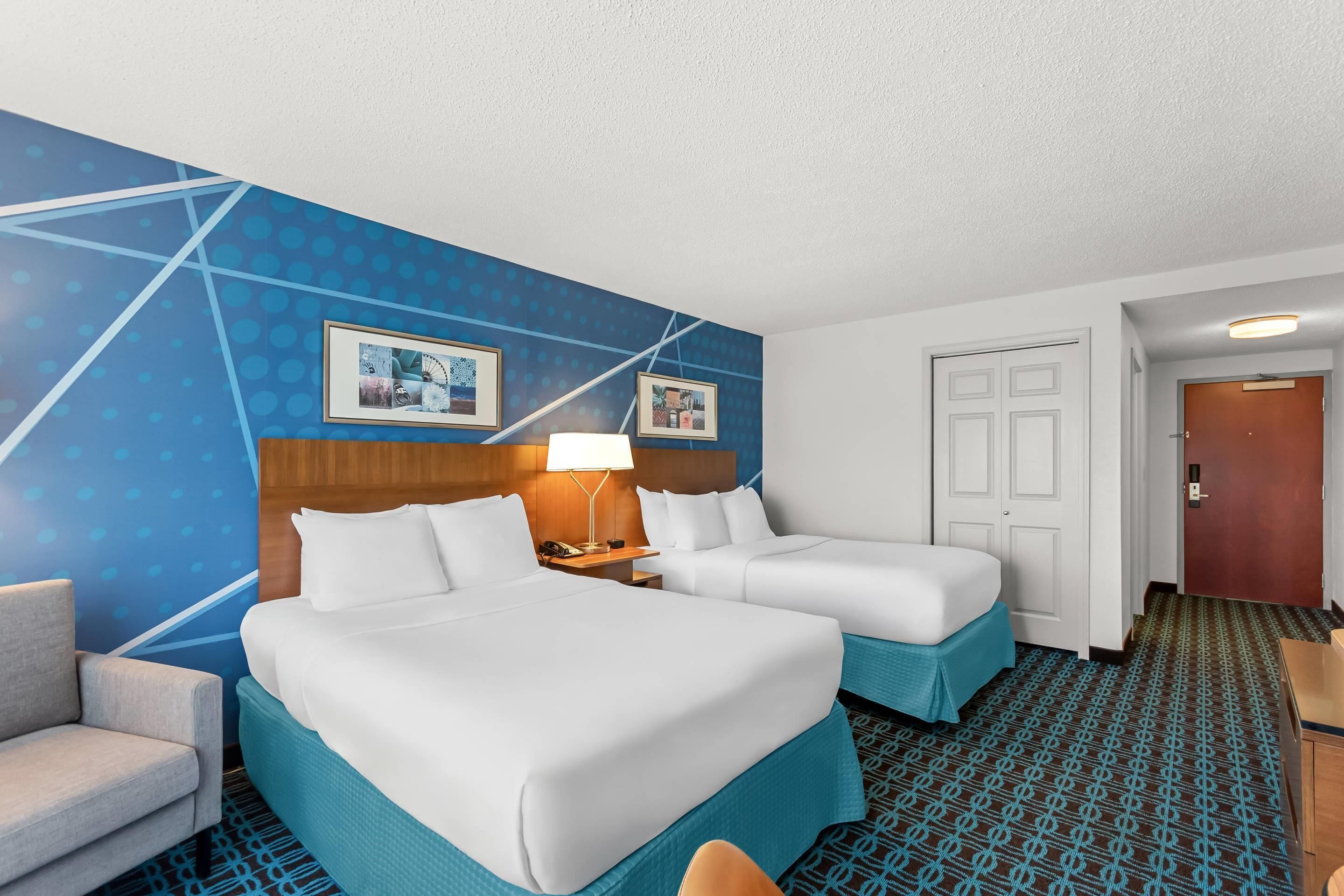 A hotel room with two beds, a desk, a chair, and a patterned carpet.