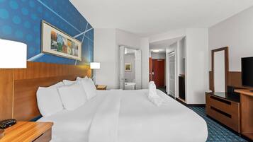 A hotel room with a large bed, a TV, a desk, and a bathroom visible through an open door.