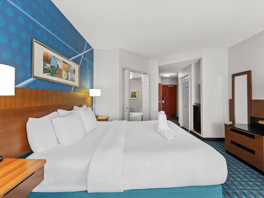A hotel room with a large bed, a TV, a desk, and a bathroom visible through an open door.