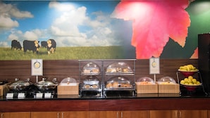 Buffet com diversos alimentos e um mural de vacas em um campo gramado.