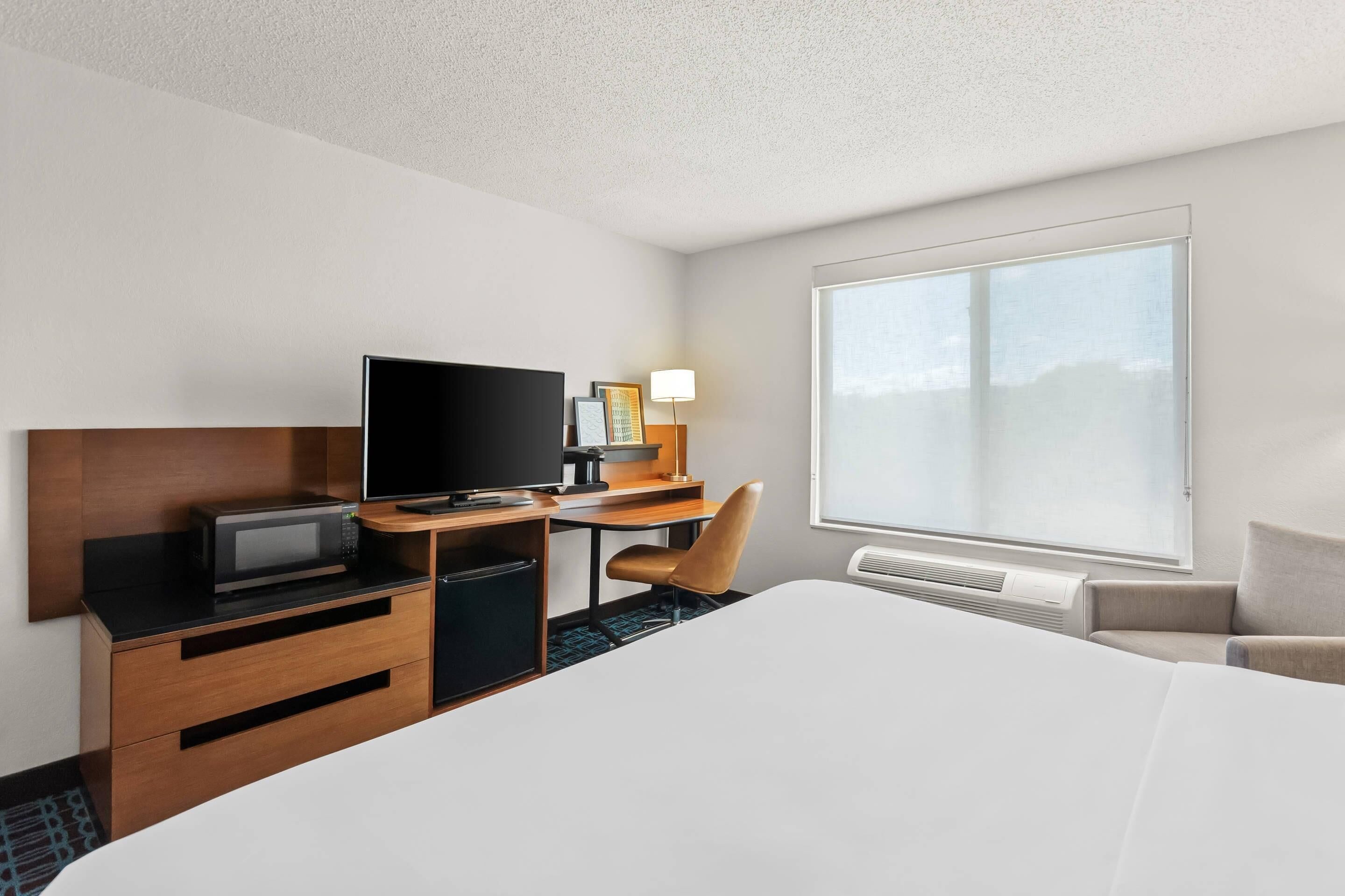 A hotel room with a large bed, a desk with a television, a chair, and a window providing a view.