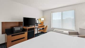 A hotel room with a large bed, a desk with a television, a chair, and a window providing a view.