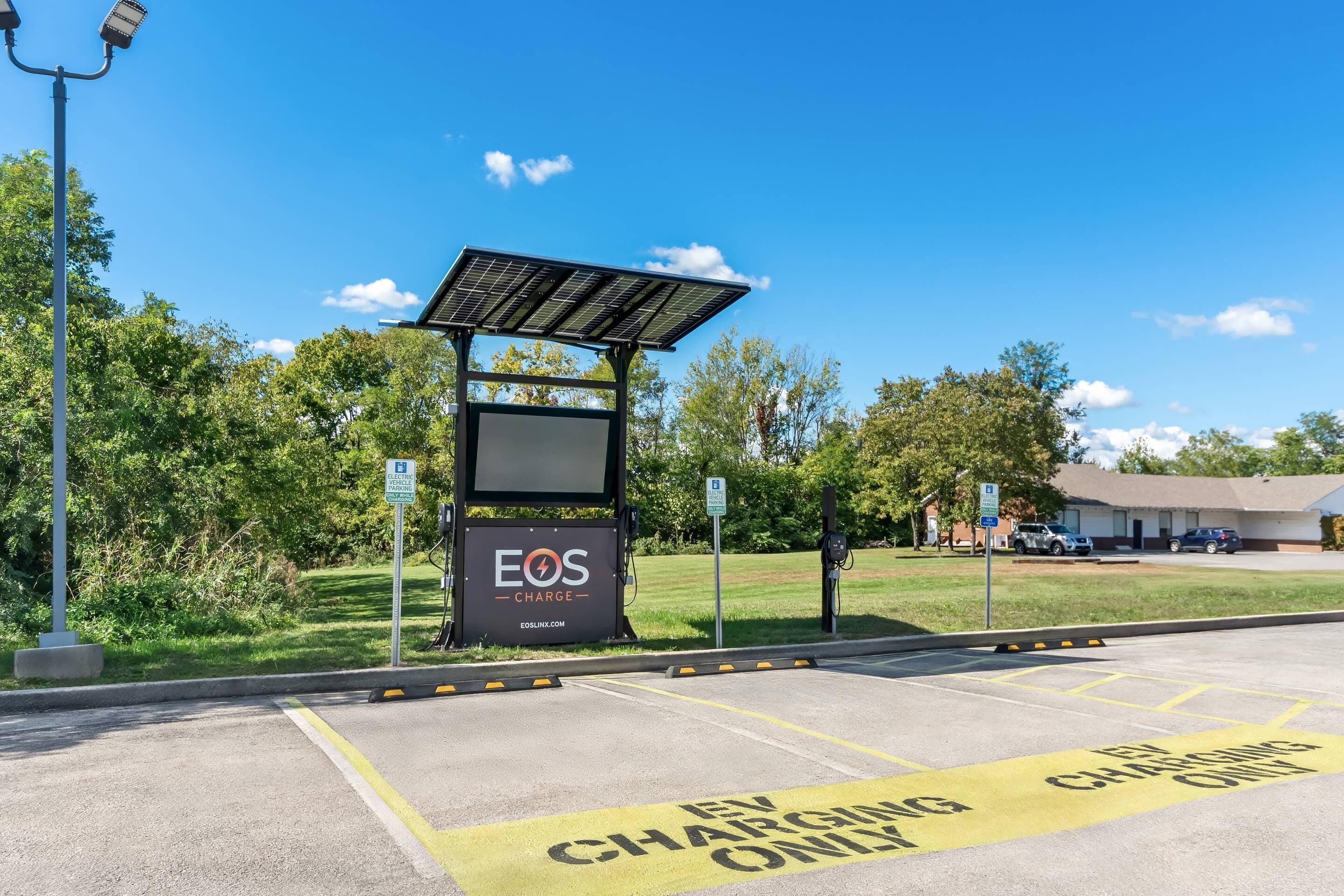 A solar-powered charging station with a sign for 'EOS CHARGE' and a parking area marked 'EV CHARGING ONLY'.