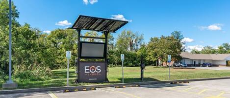 A solar-powered charging station with a sign for 'EOS CHARGE' and a parking area marked 'EV CHARGING ONLY'.