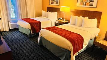A hotel room with two beds, a bedside table with a lamp, a phone, and a window with curtains.