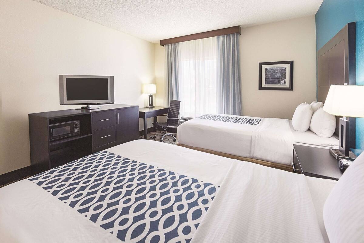 A hotel room with two beds, a desk, a television, a lamp, and a picture on the wall.